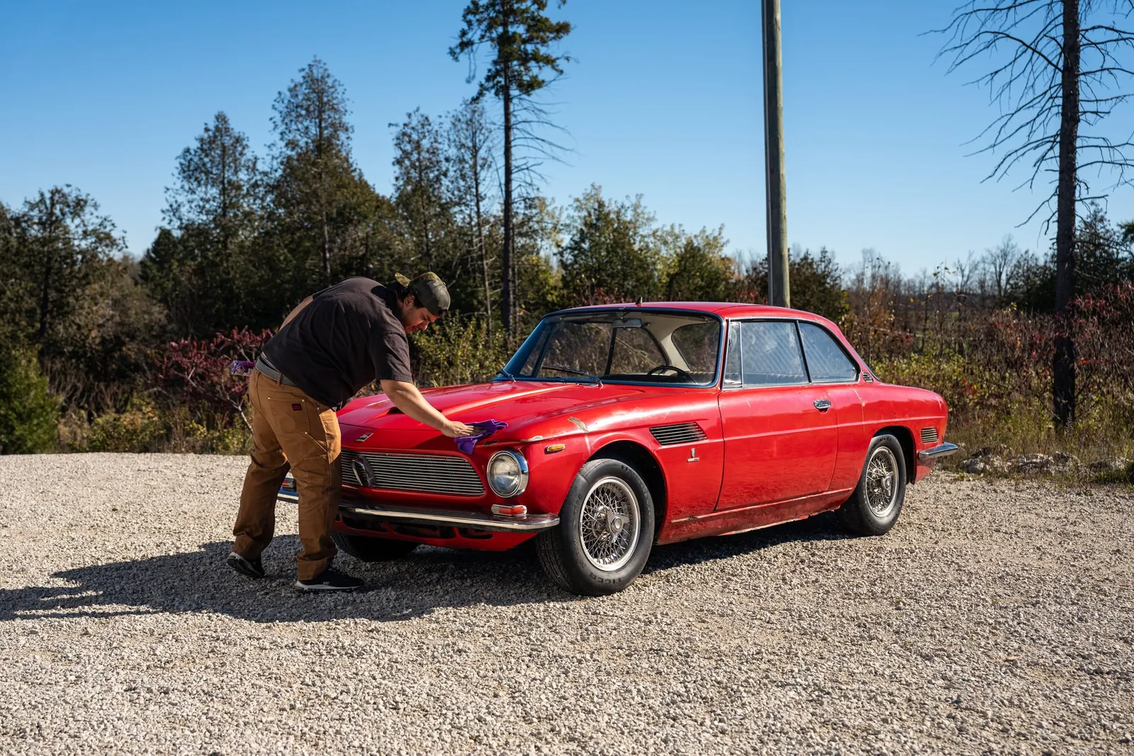 Johnnie hand-finishing a red classic coupe on a gravel drive