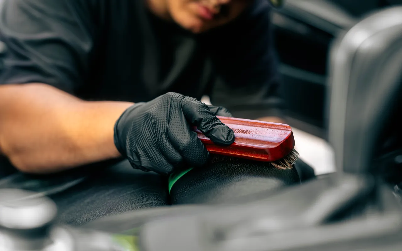 Hard-bristle brush scrubbing contaminants out of a black leather seat