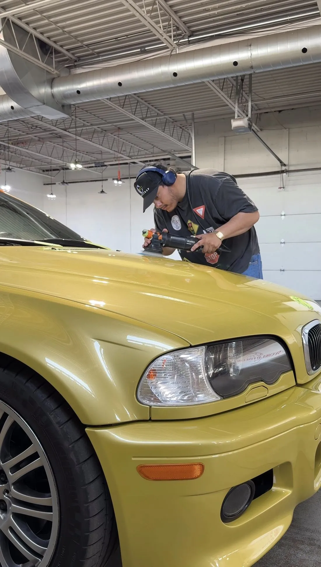Machine polishing the hood of a yellow BMW M3
